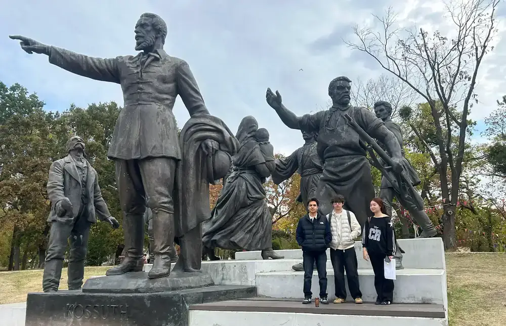 Three AIC students standing beside the Kossuth sculpture group in Orczy Park.